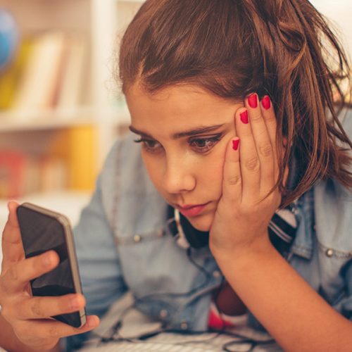 Teenage girl lying on bed in her room and checking smart phone.