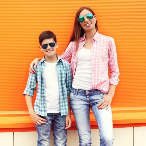 Happy mother and son teenager wearing a checkered shirt and sunglasses in city over orange background